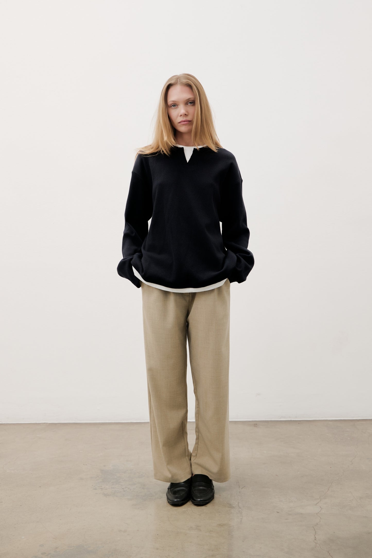 Person wearing a black sweater and beige pants against a white background