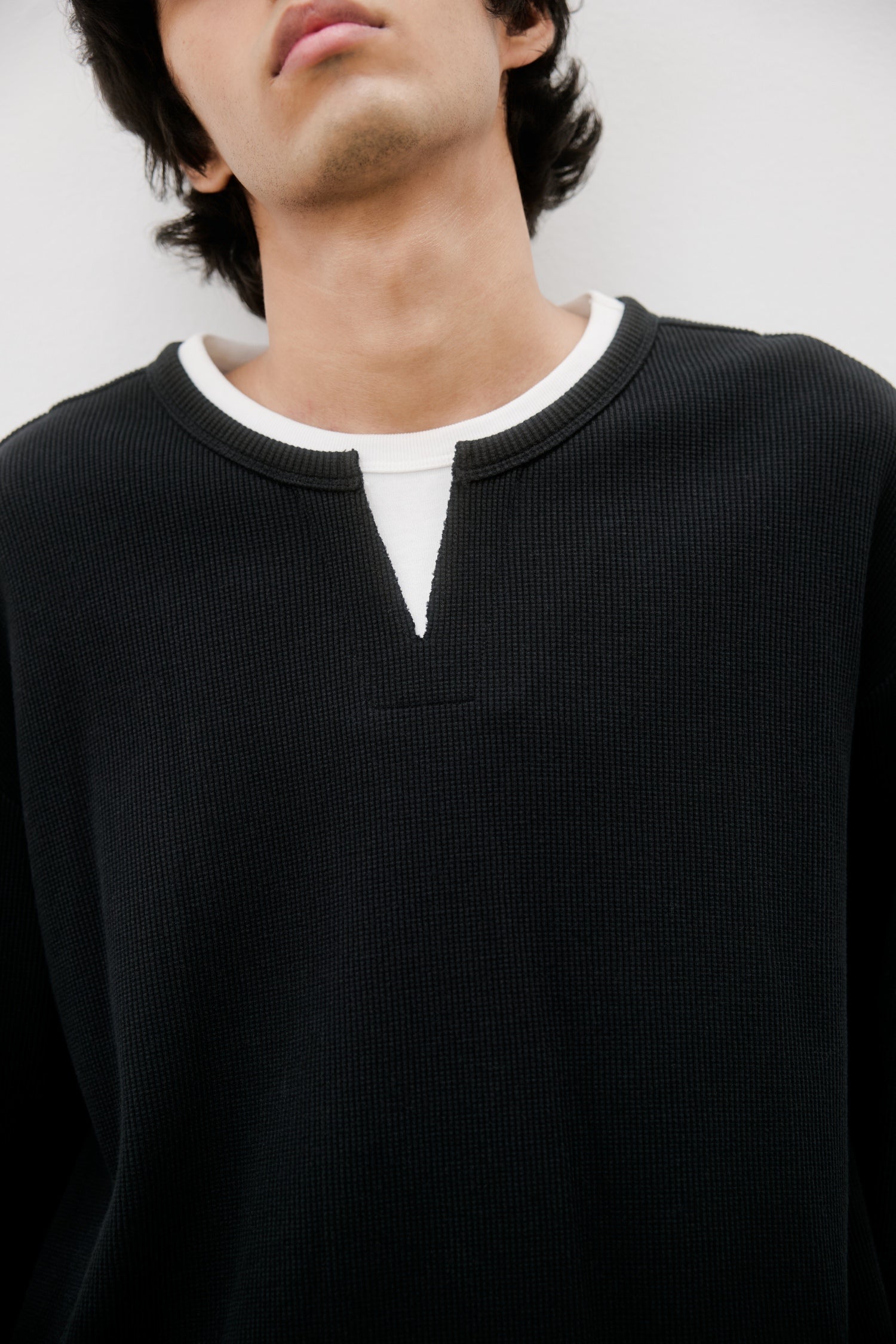 Model is wearing a black sweater with a white collar against a plain background