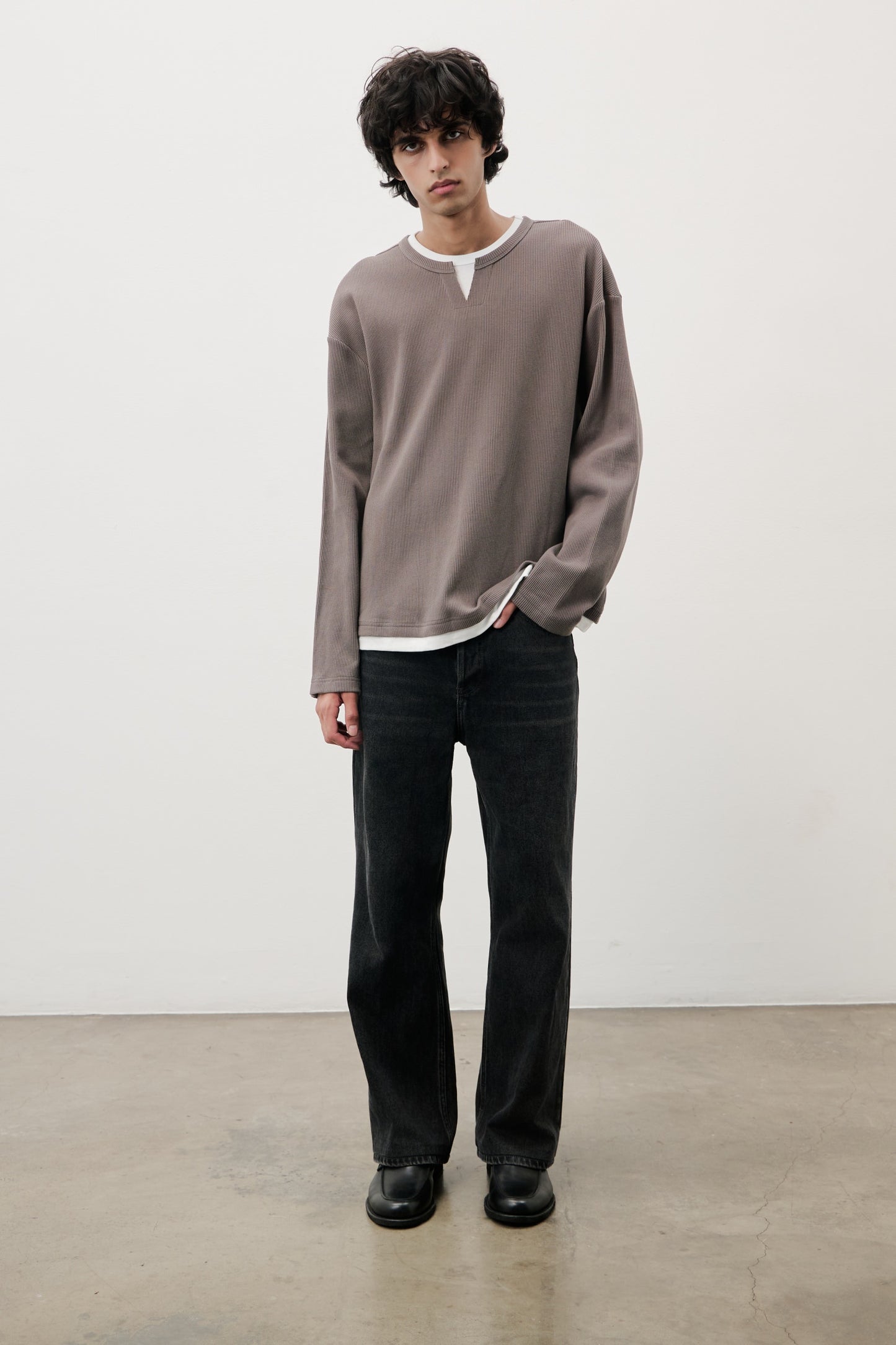 Man wearing a brown long-sleeve shirt and black pants against a white background