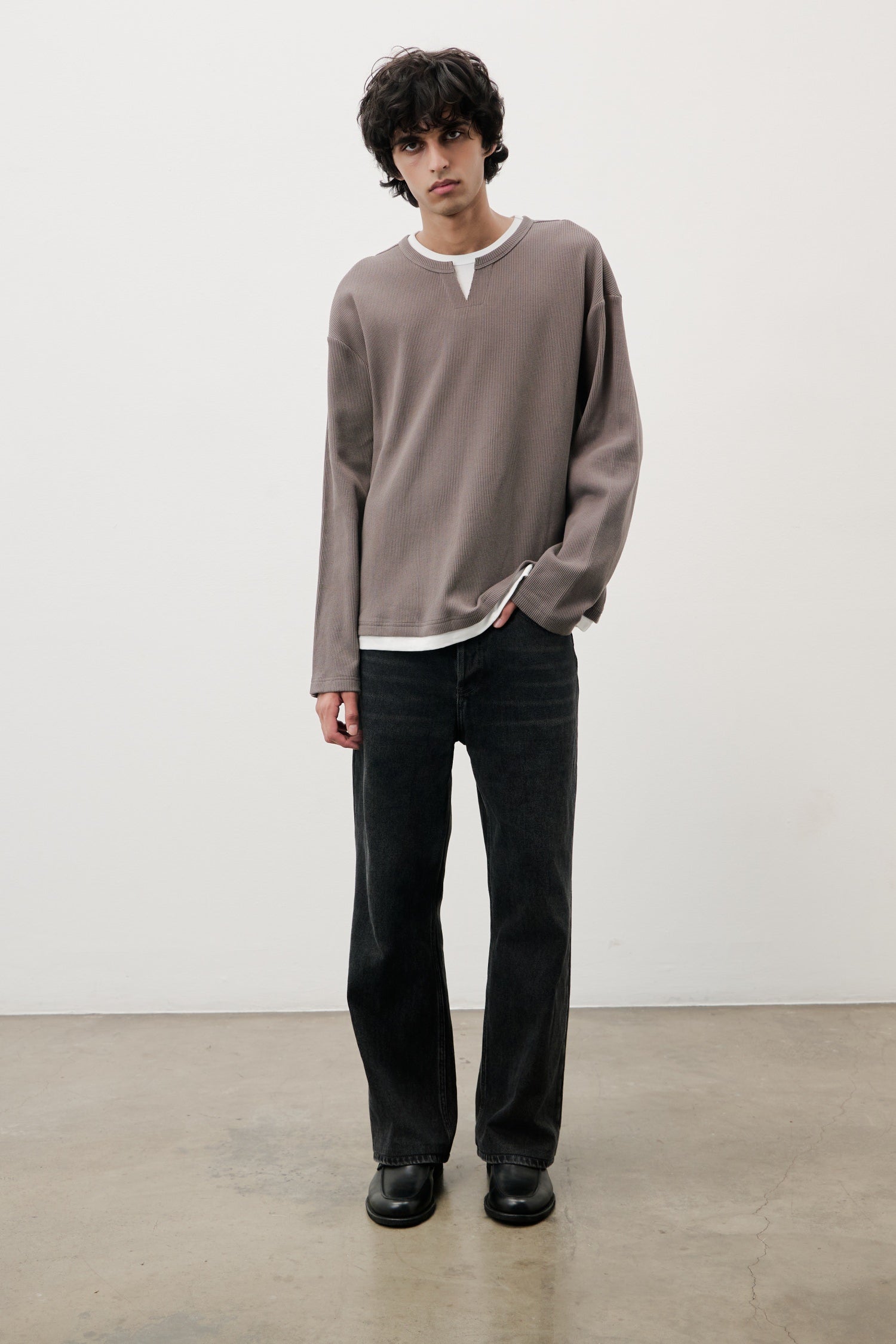 Man wearing a brown long-sleeve shirt and black pants against a white background